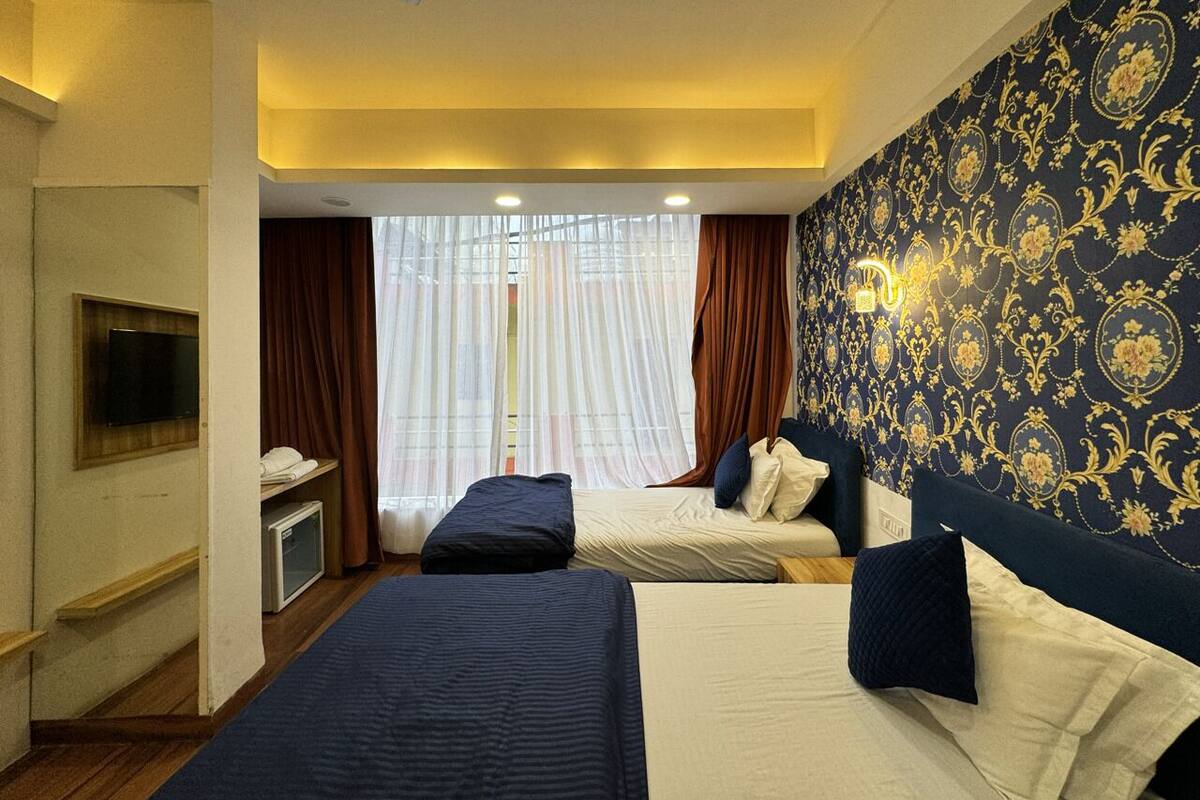 Quarto de hotel com duas camas, televisão, secretária pequena e janela com cortinas.