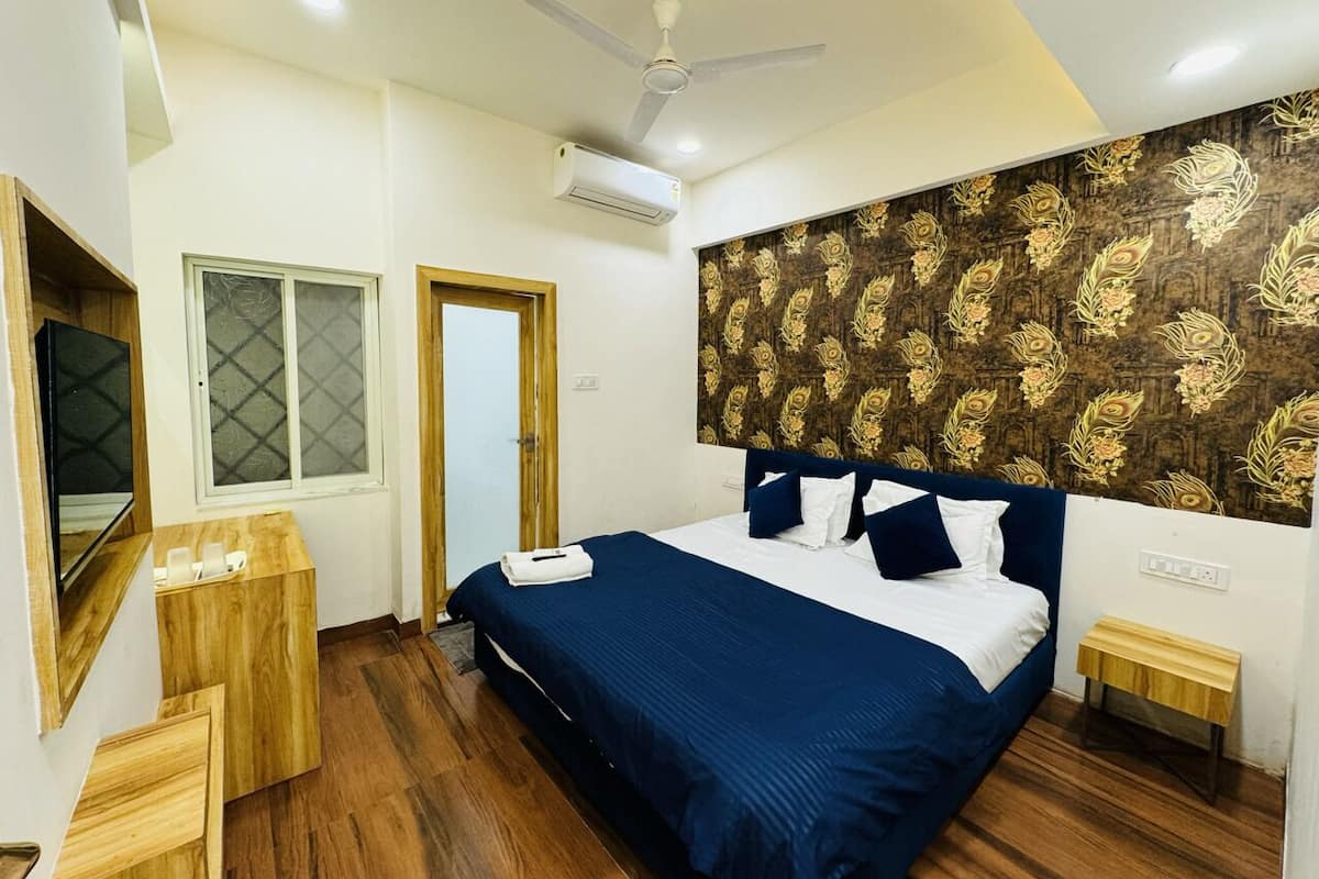 Quarto com cama, piso de madeira, ventilador de teto, ar condicionado, janela e parede com padrão floral.