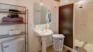 A bathroom with a pedestal sink, a mirror, a shower with a glass door, a toilet, and a laundry basket. - Casa las Mariposas Bungalow 9 (Los Ayala)