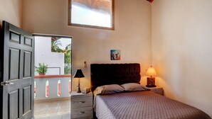 A bedroom with a bed, a nightstand, a lamp, a window, and a door. - Casa las Mariposas Bungalow 9 (Los Ayala)