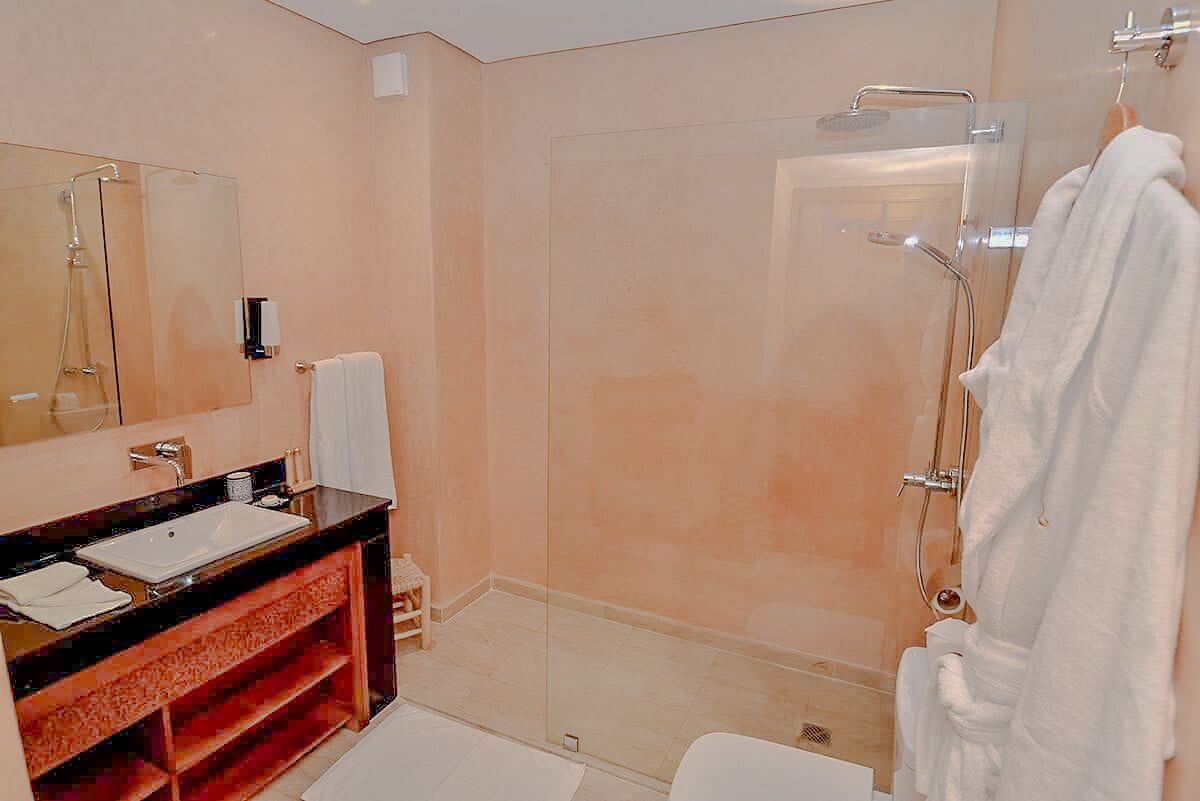 A modern bathroom with a glass shower enclosure, a vanity with a sink and mirror, and a white bathrobe hanging on the wall.