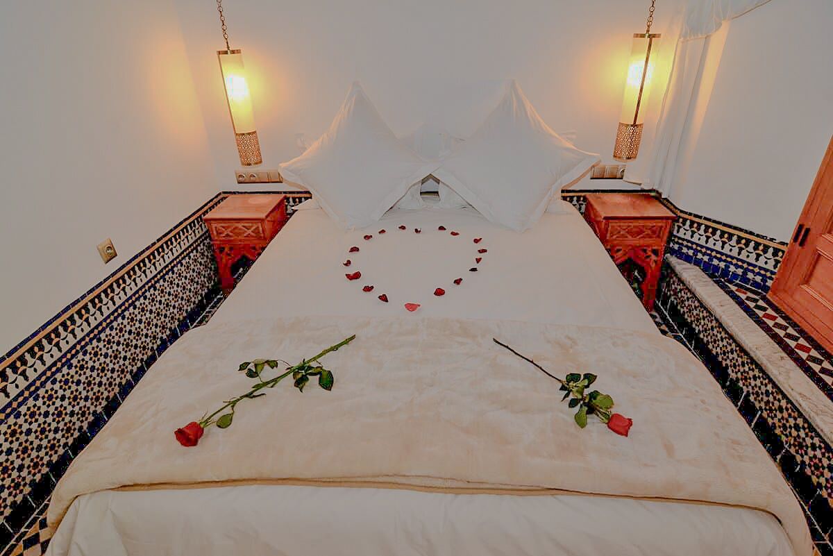 A room with a bed centered, flanked by patterned walls and two wall-mounted lamps.