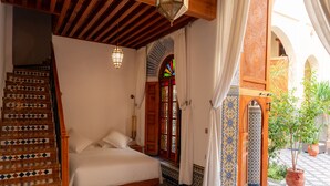 A bedroom with a bed, a wooden staircase, and a view of an outdoor courtyard with a potted plant. - Riad Al Ansari (Fes)