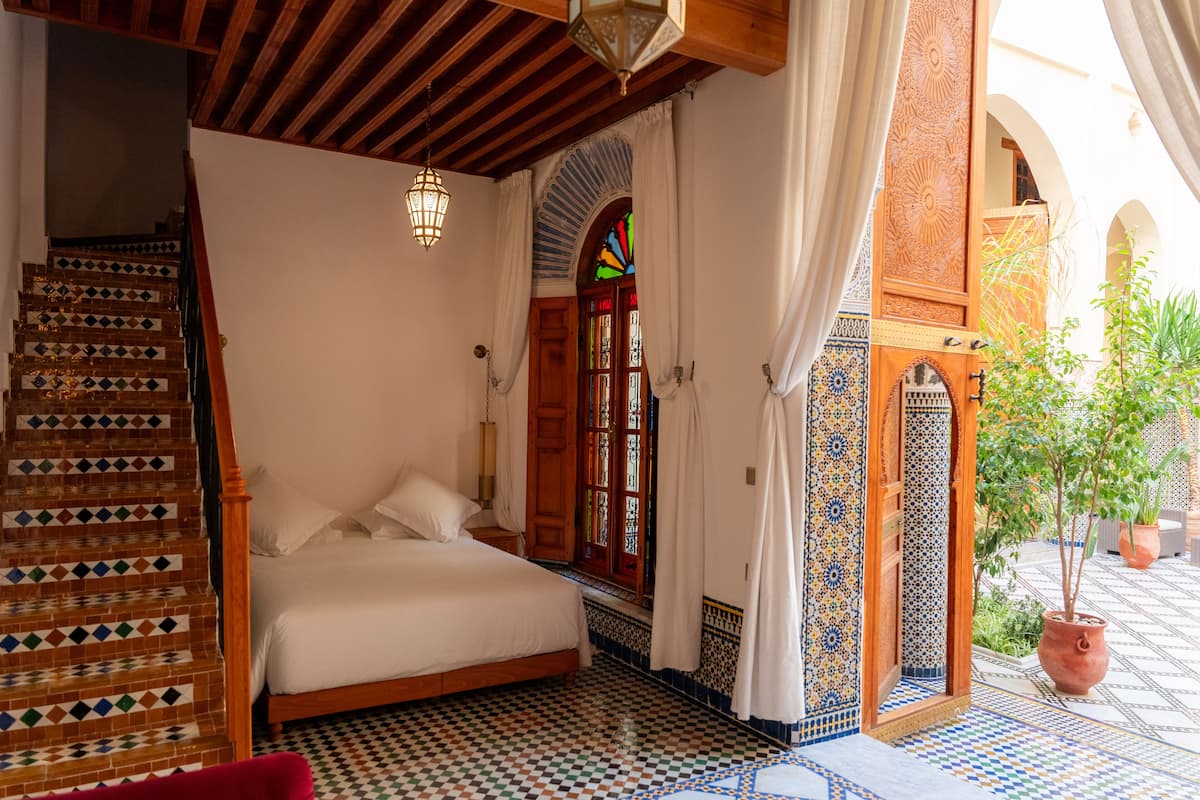 Ein Schlafzimmer mit Bett, einer Holztreppe und Blick auf einen Innenhof mit einem Blumentopf.