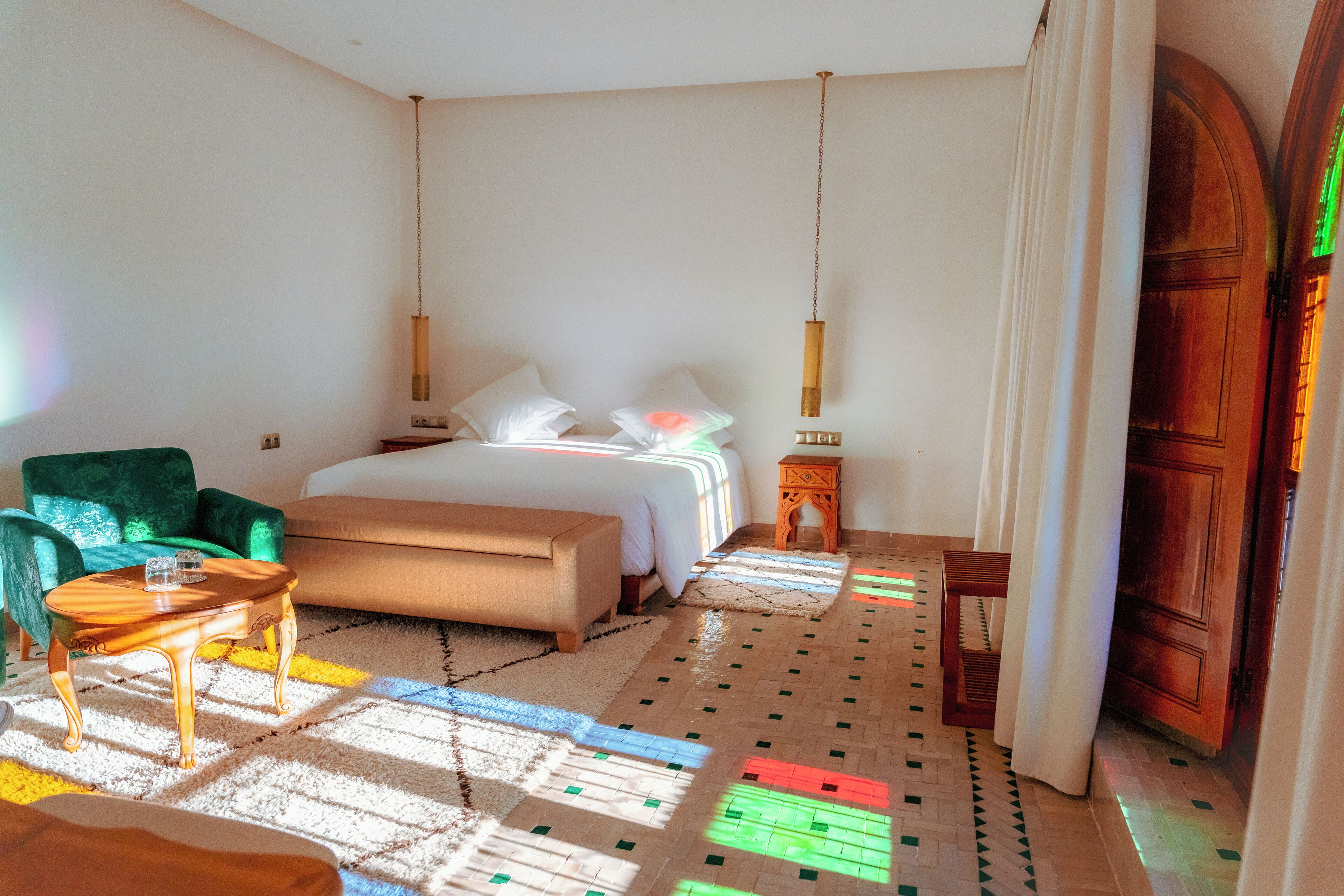 Een slaapkamer met een bed, een groene fauteuil, een houten bijzettafeltje en een klein houten kastje.