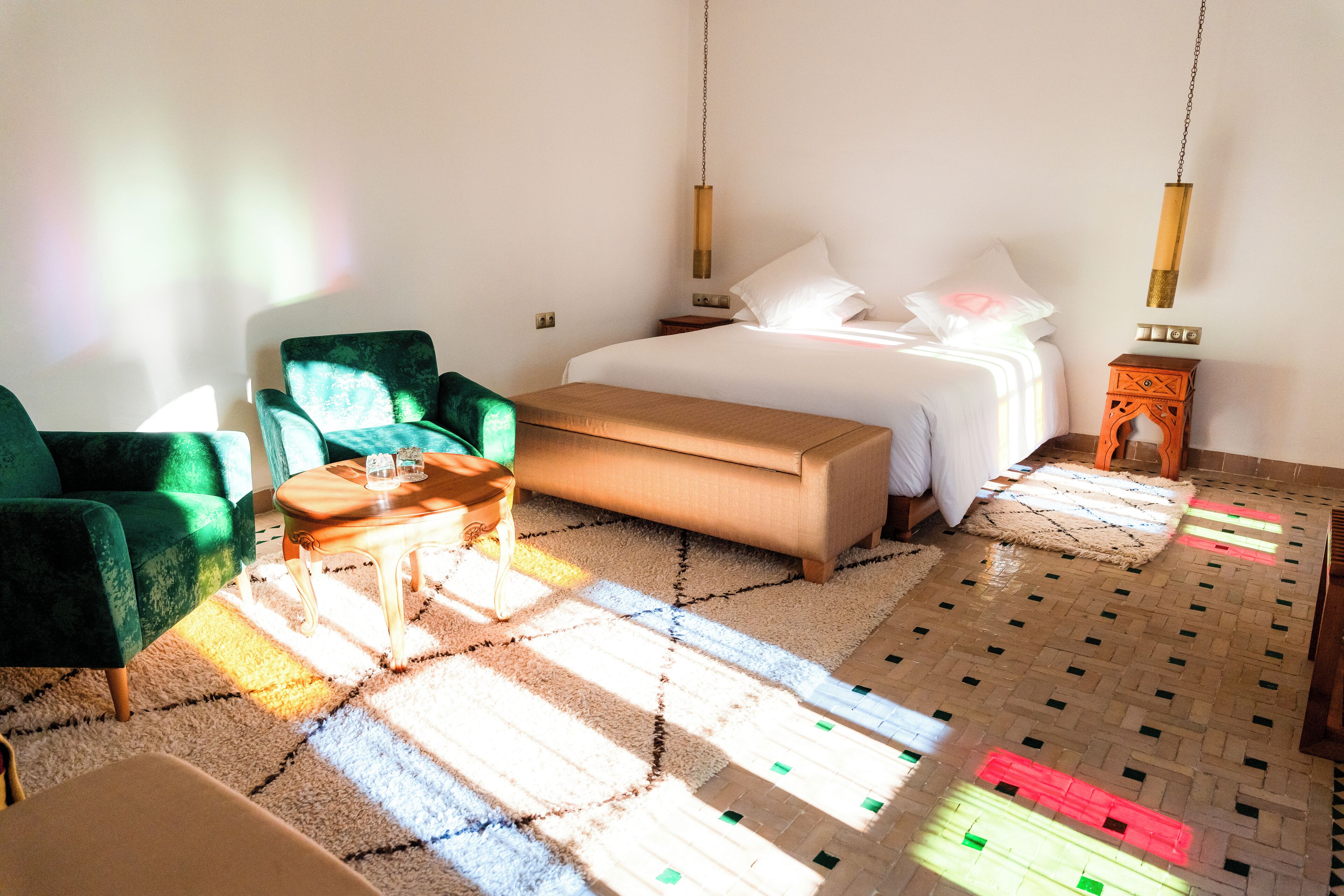 Une chambre à coucher avec un lit, un fauteuil vert, un banc en bois et une petite table.