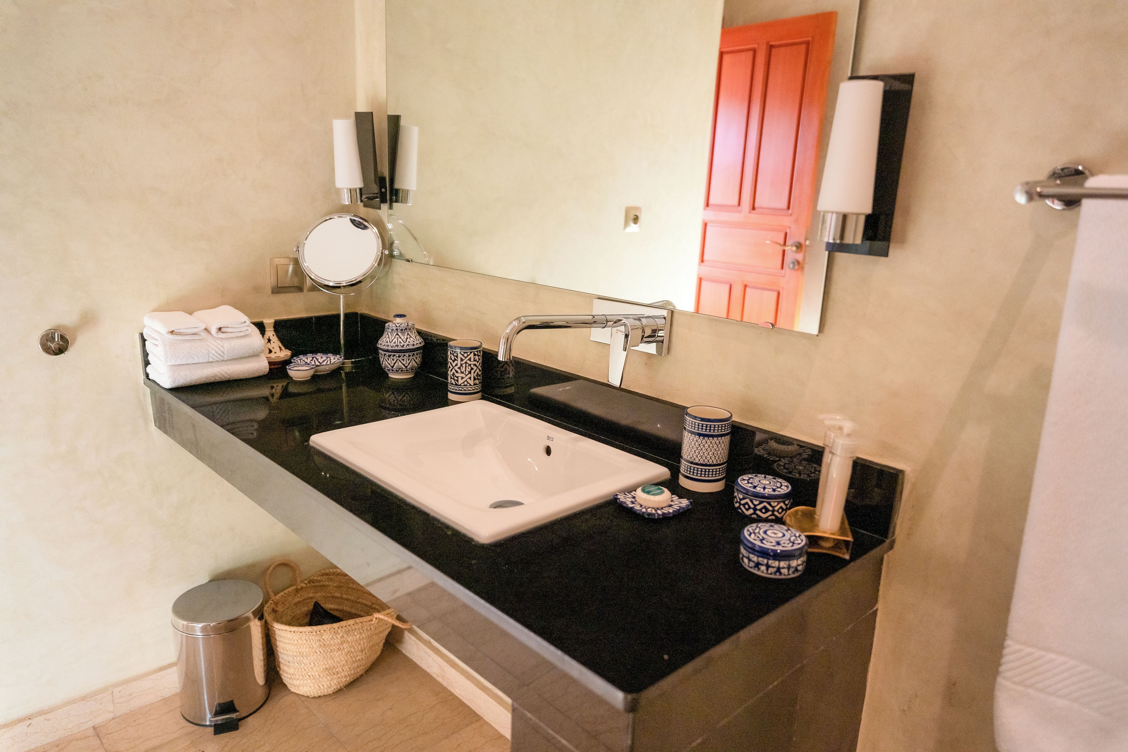 A bathroom with a black countertop, white sink, and a mirror. There are decorative items and a trash can.