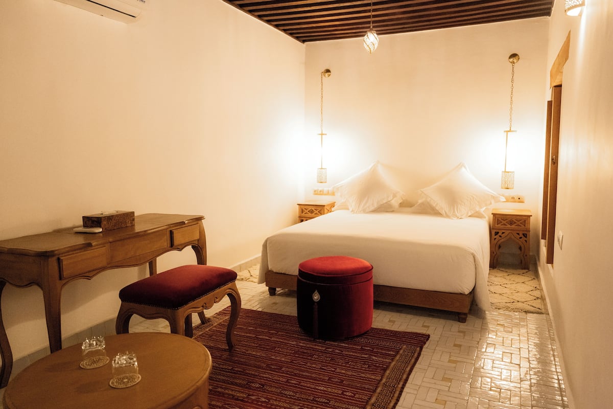 Ein Schlafzimmer mit einem Bett, Nachttischen, einem Schreibtisch und einem runden Tisch mit Gläsern.