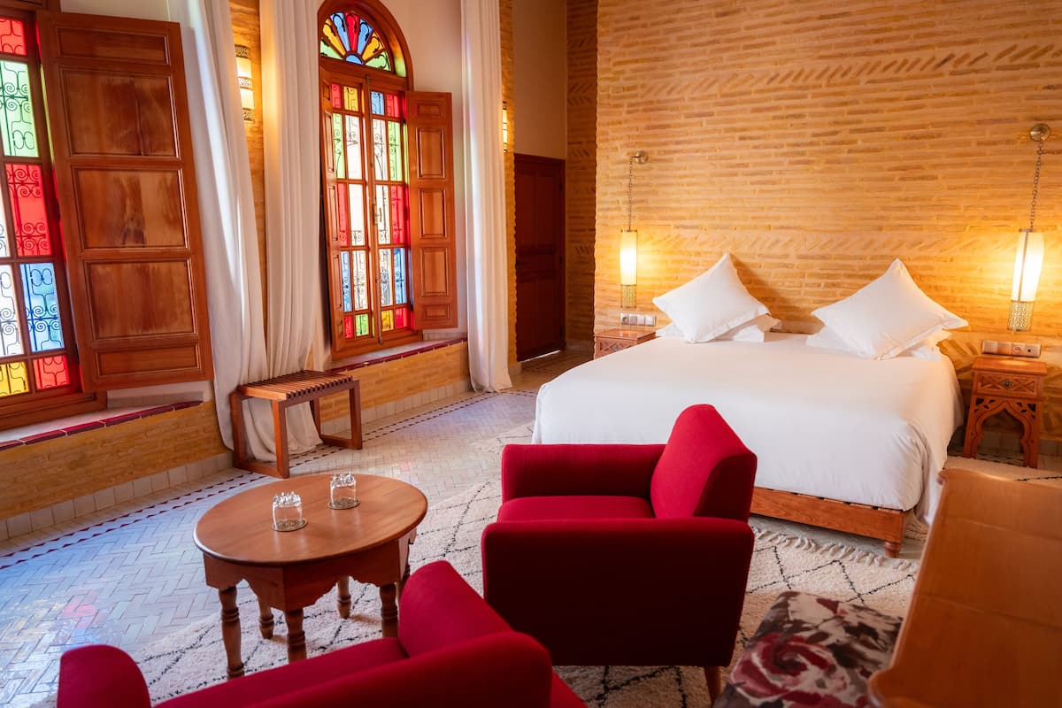 Ein Hotelzimmer mit einem großen Bett, zwei Nachttischen, einer Holzbank, einem runden Tisch und roten Sessel.