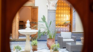 An interior courtyard with a fountain, potted plants, and a seating area with a patterned wall in the background. - Riad Al Ansari (Fes)