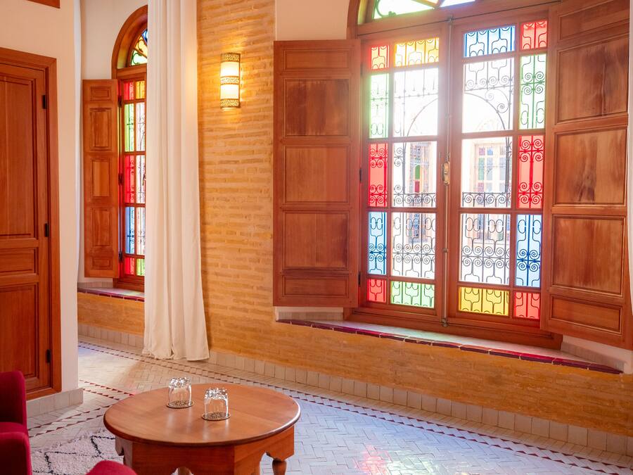 Un hall d’hôtel avec des boiseries, des vitraux et une table ronde entourée de chaises.
