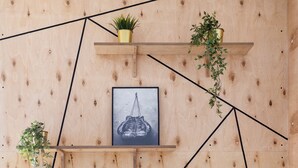 A modern room with a wooden wall, geometric black lines, and shelves with plants and a framed picture. - EASY RENT Apartments - Smart 005 (Lublin)