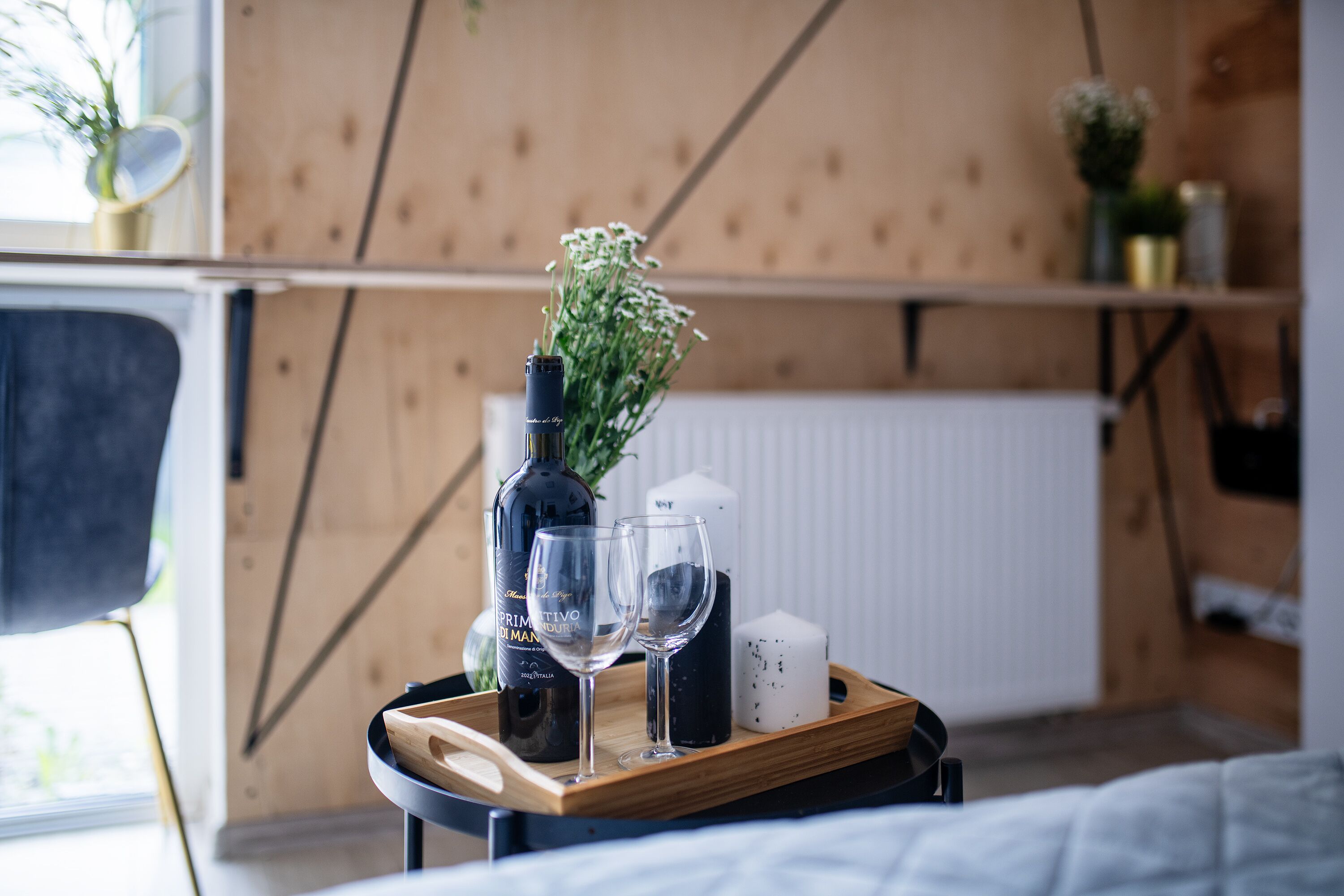 Ett träbricka med en flaska, två glas och ett ljus på ett sängbord.