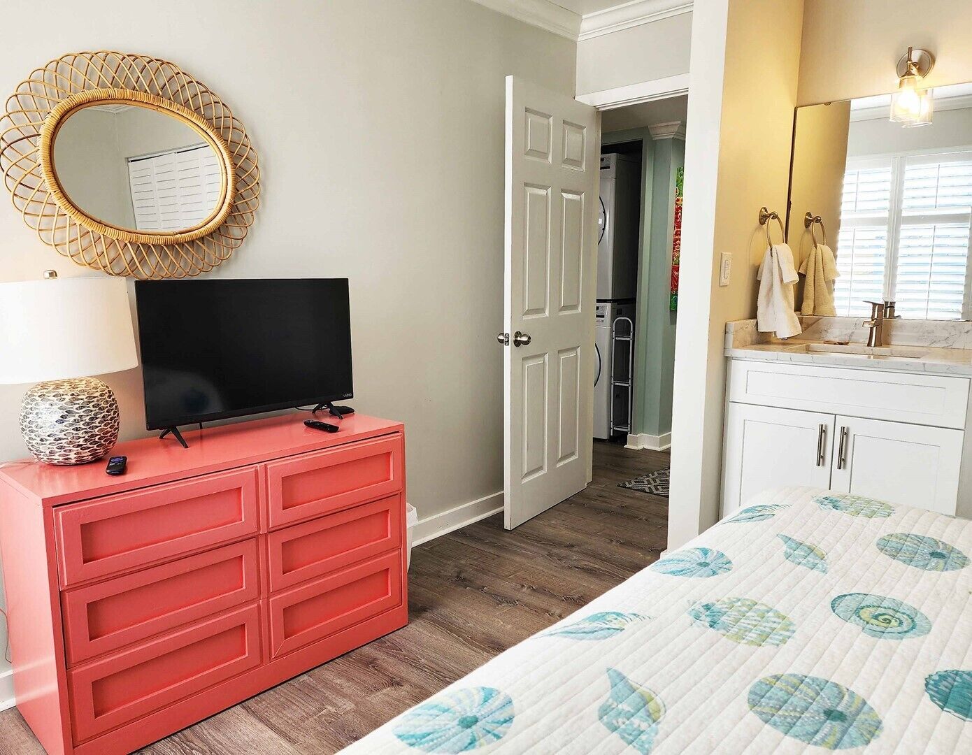 Een slaapkamer met een rode dressoir, een televisie, een ronde spiegel en een bed met een bloemenquilt.