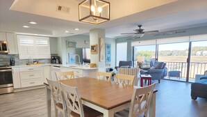 A modern kitchen with white cabinets, a dining table with chairs, and a large window overlooking a scenic view. - Inlet Point 14A offers Beautiful Marsh Views and Easy Creek Access (Pawleys Island)
