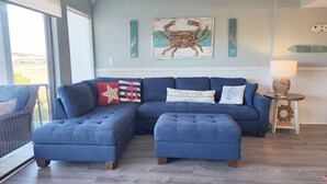 A living room with a blue sectional sofa, a matching ottoman, and nautical-themed decor. - Inlet Point 14A offers Beautiful Marsh Views and Easy Creek Access (Pawleys Island)