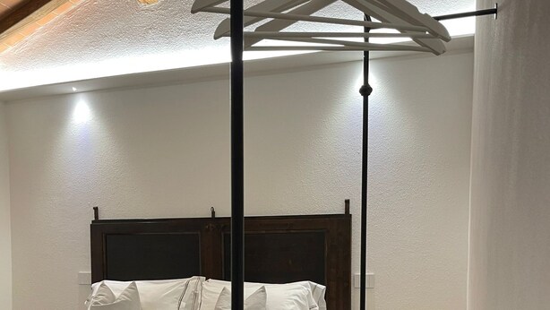 A bedroom with a wooden headboard, a bed with white bedding, a small round table, and a bench.