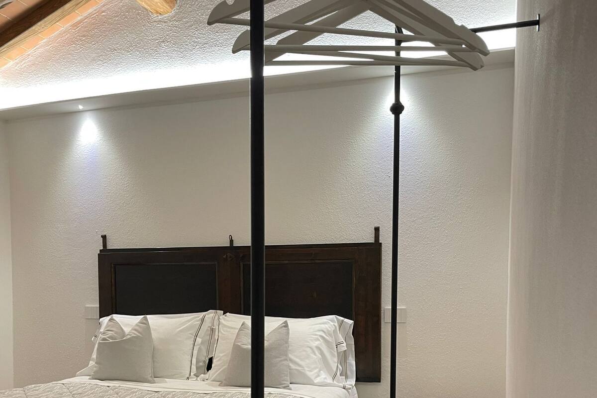 A bedroom with a wooden headboard, a bed with white bedding, a small round table, and a bench.