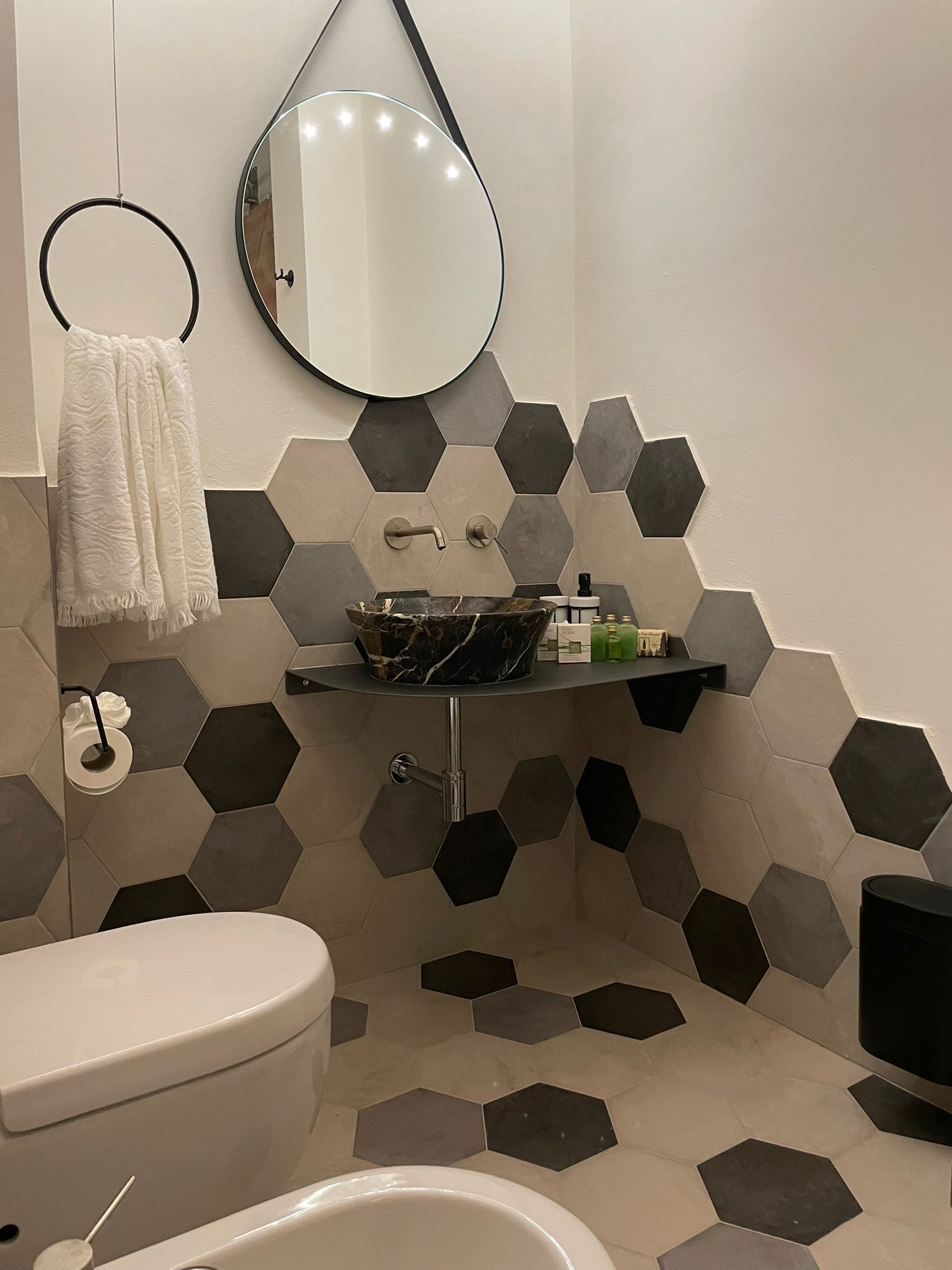 Een badkamer met toilet, wastafel en spiegel. De muren zijn betegeld met een honingraatpatroon.
