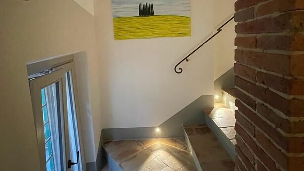 A staircase with a brick archway, a painting of a field, and a door with a window. - MontepulcianoLettings (Montepulciano)