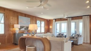 Un vaste espace de vie avec des murs en bois, un grand canapé, une table ronde et une vue sur l’océan.
