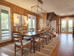 A dining area with a wooden table and chairs, a staircase, and large windows.