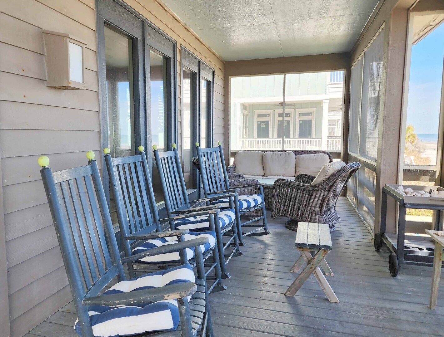 Un espace extérieur aménagé avec des meubles de jardin, comprenant des chaises bleues et un canapé en osier, offrant une vue sur un immeuble et une plage.