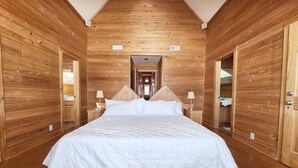 Une chambre aux murs lambrés, avec un grand lit, deux tables de chevet et une porte sur un des côtés.