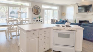 Une cuisine moderne avec des meubles blancs, une cuisinière encastrée et un coin repas avec des chaises blanches.
