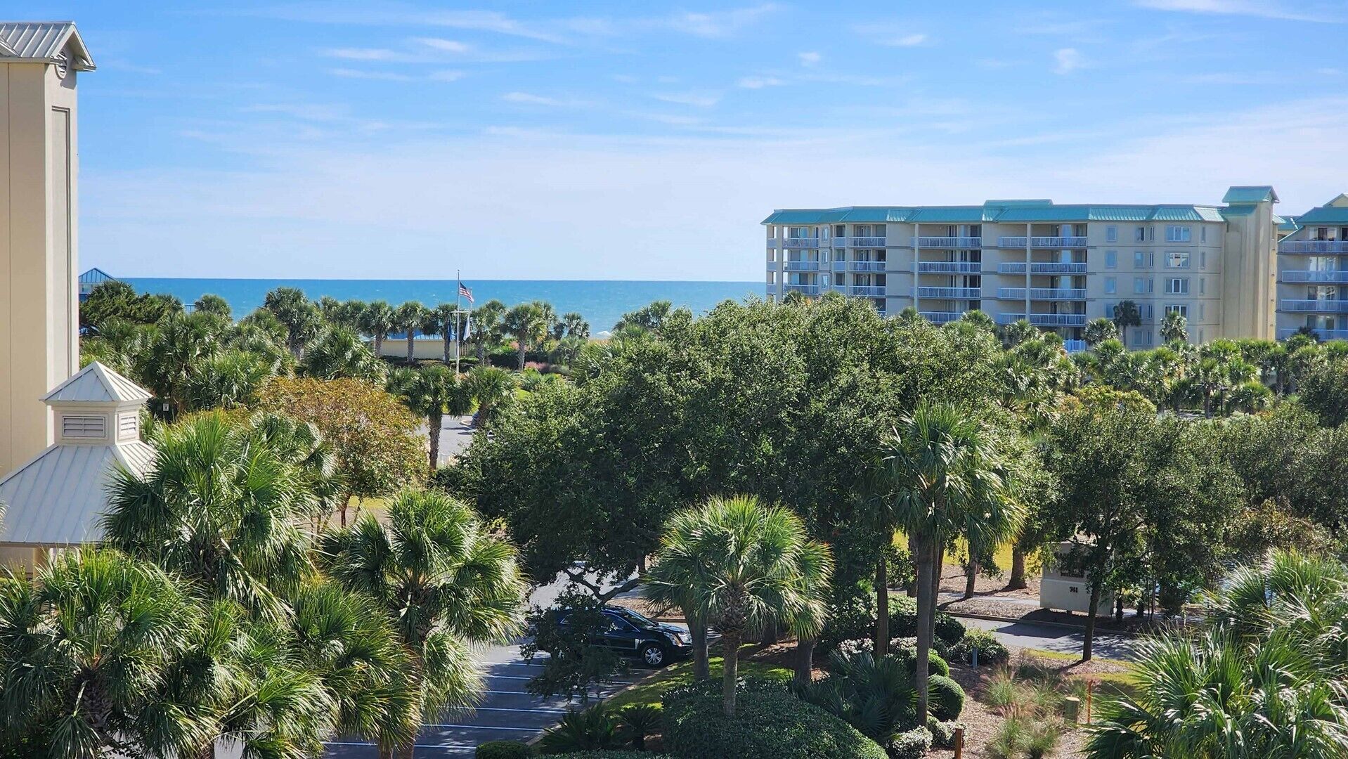 Un resort con vista sull'oceano, palme e un edificio a più piani con balconi.