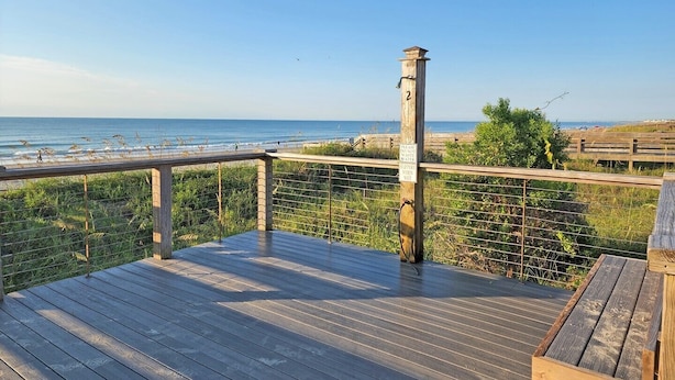 Une terrasse en bois avec une balustrade donnant sur une plage.