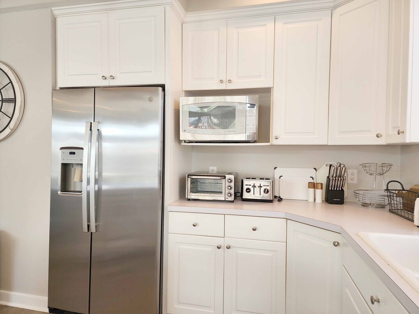 A kitchen with white cabinets, a stainless steel refrigerator, a microwave, a toaster, and a water dispenser.