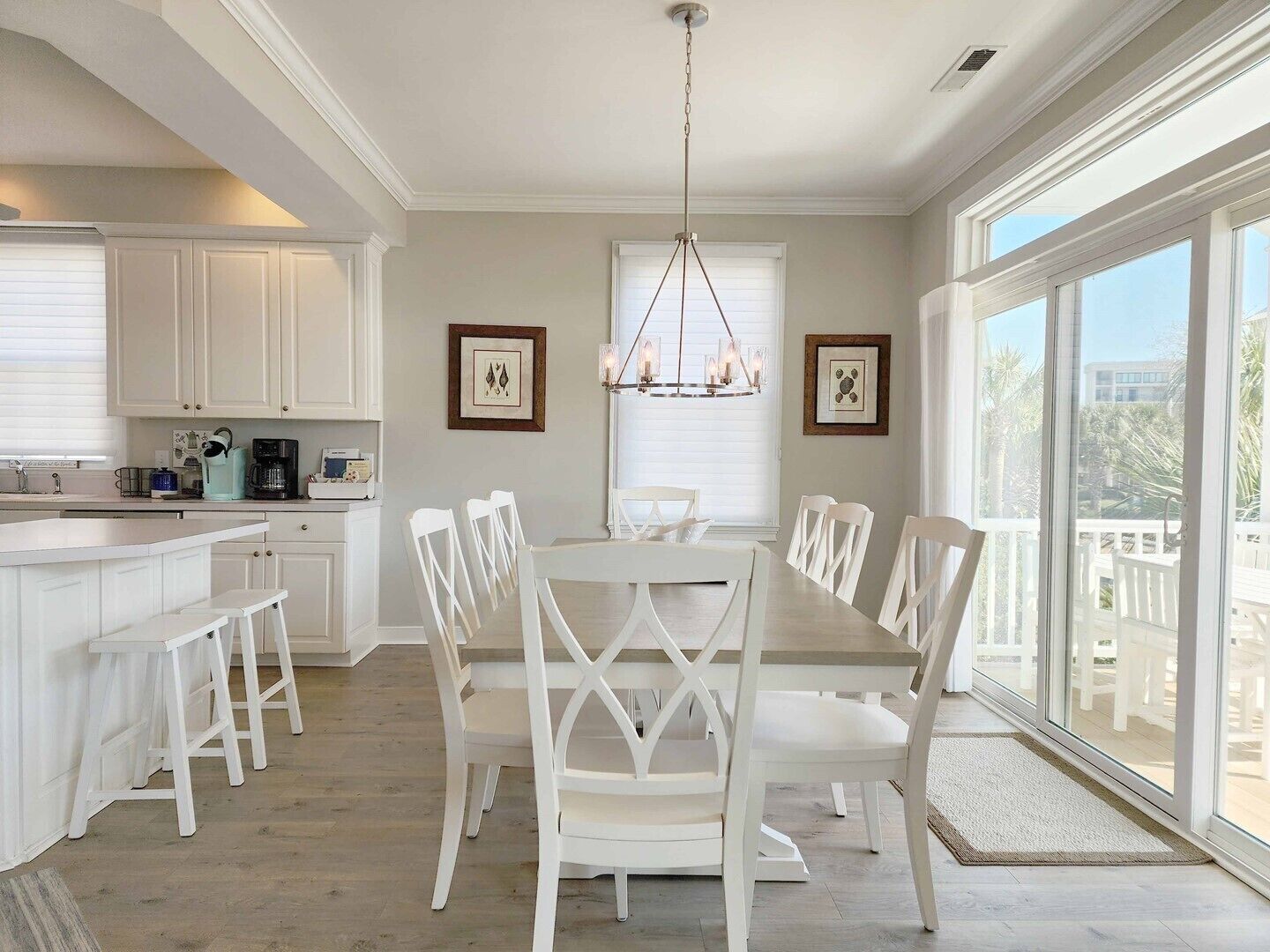 Une cuisine spacieuse avec des meubles blancs, un coin repas doté d’une grande table et de chaises blanches, et une vue dégagée grâce à de grandes fenêtres.