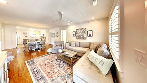 Una sala de estar amplia con sofá, reposapiés y mesa de centro, un comedor con sillas y una mesa, y una cocina al fondo.