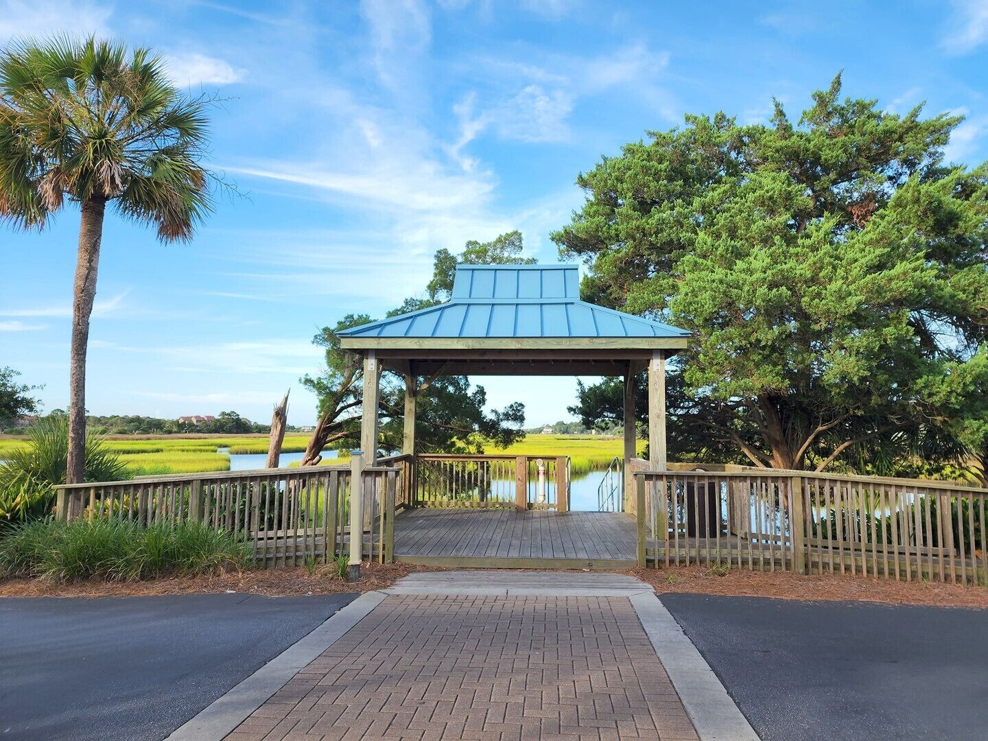 A gazebo with a blue roof, surrounded by a wooden fence, and a paved walkway leading to it.