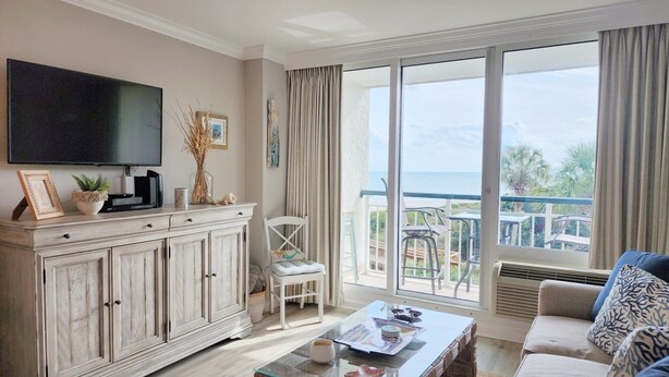 Una sala de estar con televisor, una mesa de comedor, un sofá y un balcón con vista al mar.