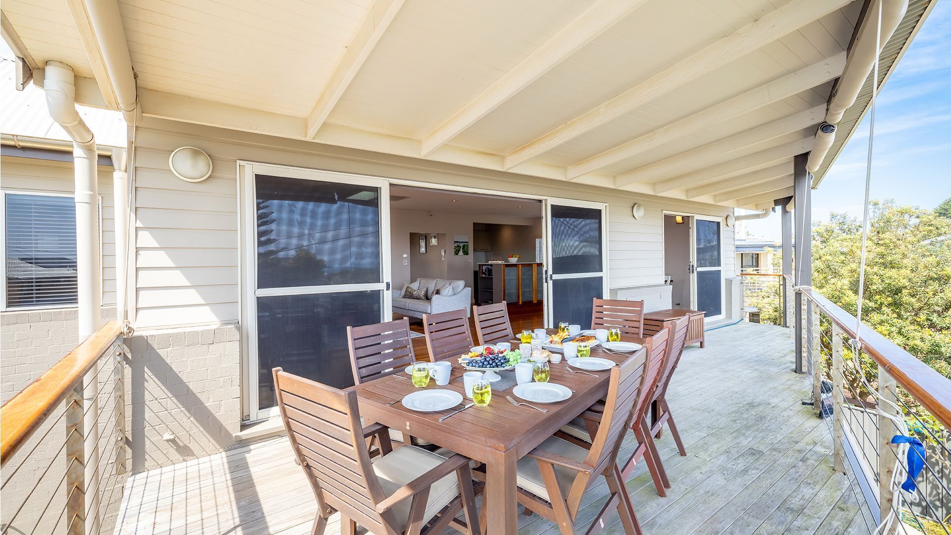 A covered outdoor dining area with a wooden table set for four, surrounded by chairs.