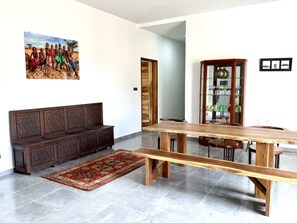 Um quarto espaçoso com um banco de madeira, uma grande mesa de jantar e um tapete vermelho estampado.