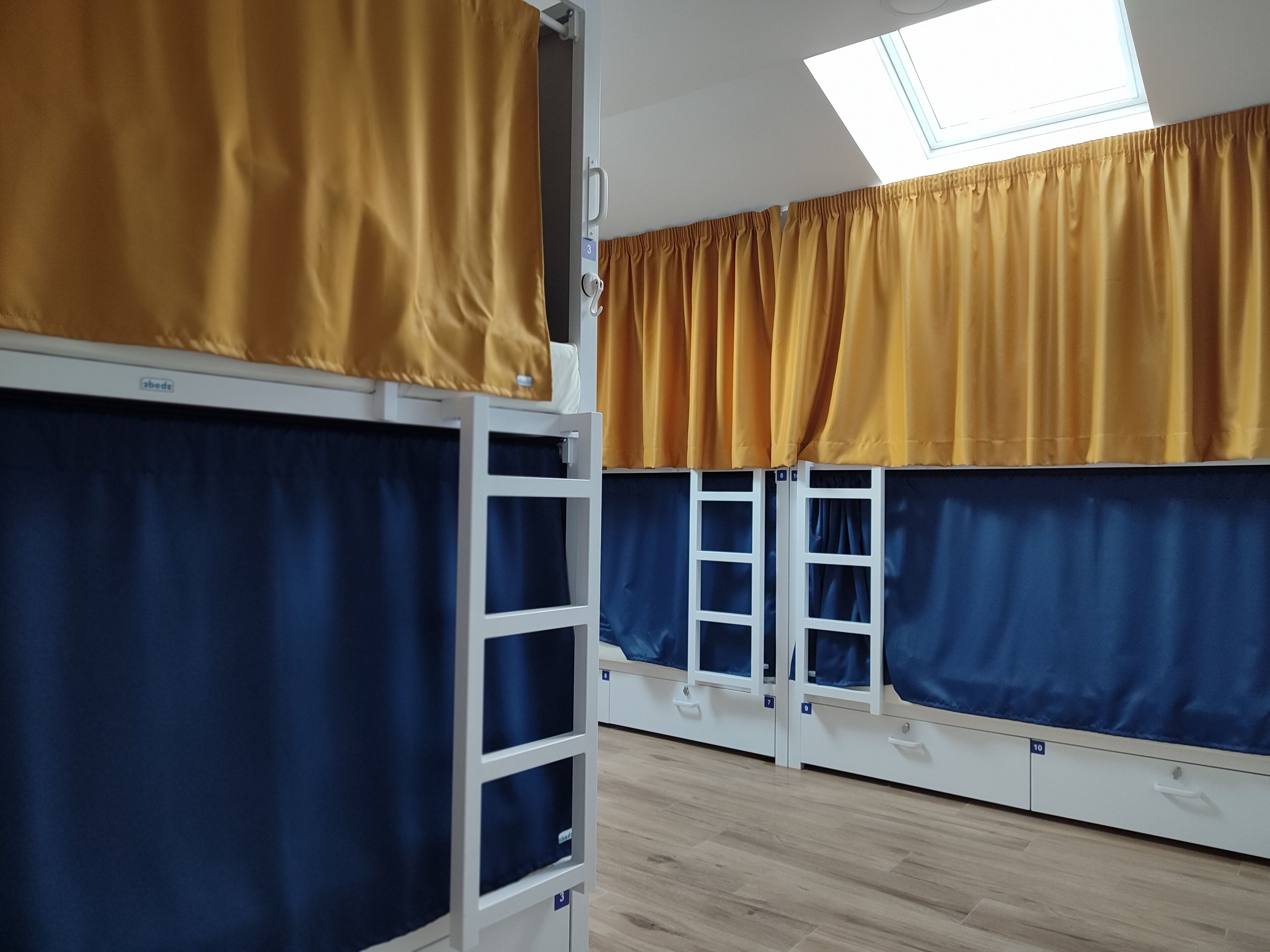 A dormitory room with bunk beds, numbered doors, and a skylight.
