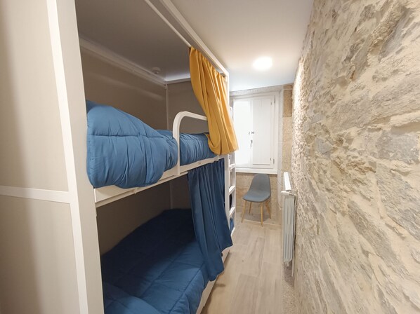 Dormitorio con literas, pared de piedra, escritorio pequeño y una silla.