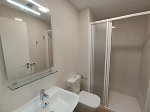 Une salle de bain moderne avec une étagère en verre au-dessus du lavabo, des toilettes et un espace douche.