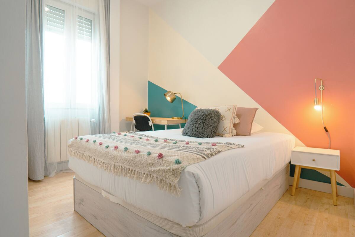 Un dormitorio con cama, mesita de noche, lámpara y escritorio con silla.