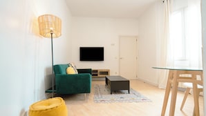 A modern living room with a green sofa, a yellow pouf, a glass coffee table, a floor lamp, and a TV mounted on the wall. - Live It Madrid Chamberi (Madrid)