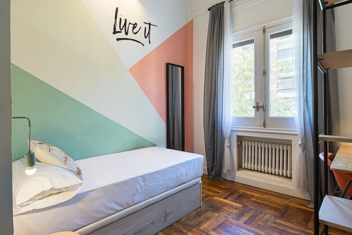 Un dormitorio con cama, un radiador, una ventana con cortinas y una pared con diseño geométrico.