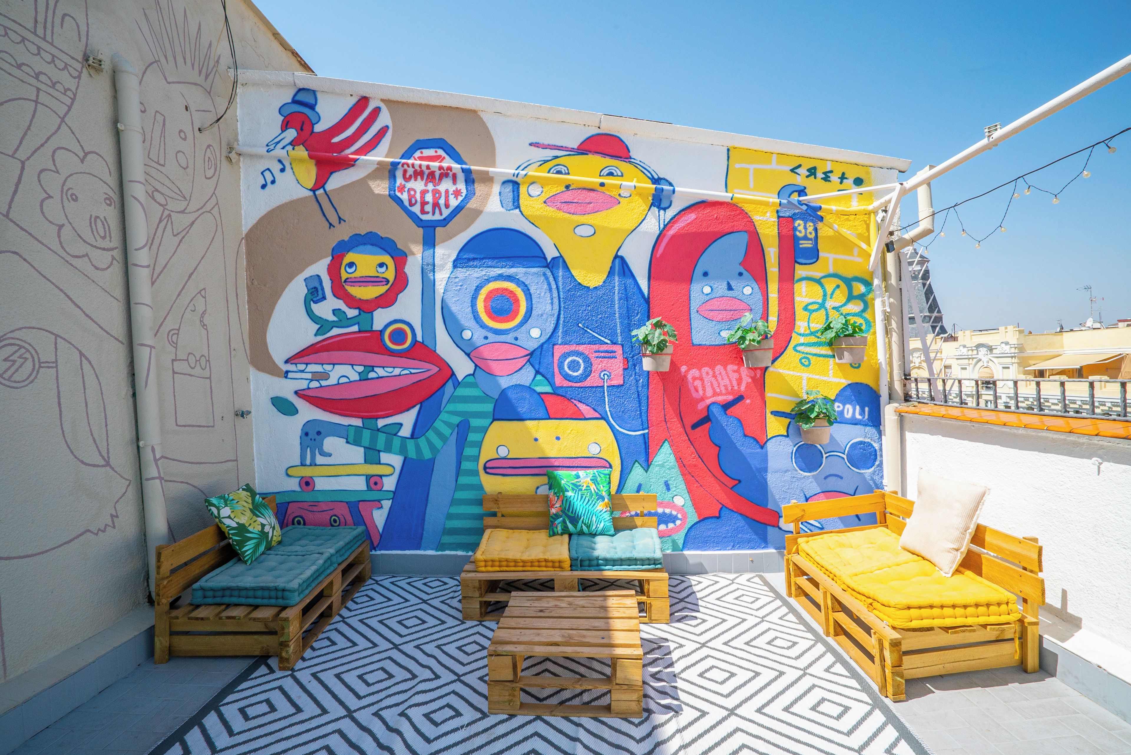A colorful mural with abstract figures and text, wooden furniture, and a patterned floor.