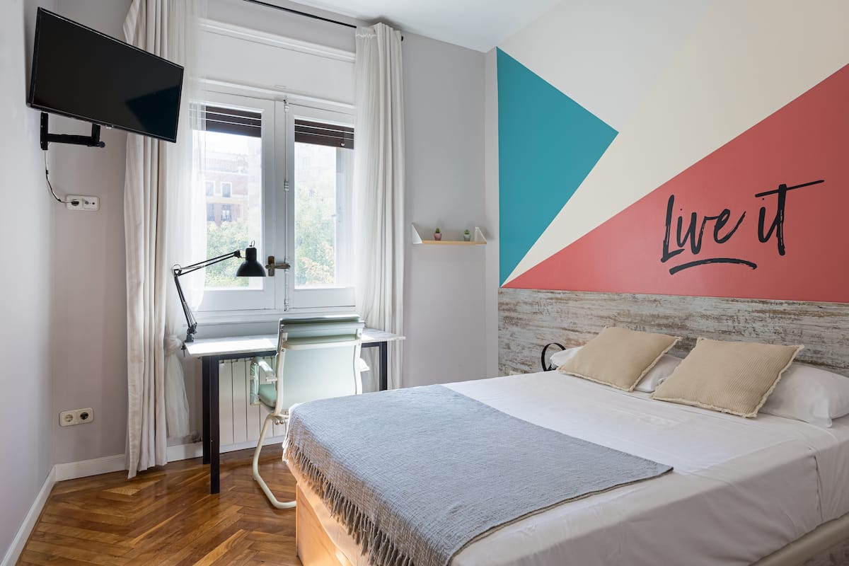 Un dormitorio con cama, escritorio, televisor y un cuadro motivacional que dice 'Live it'.