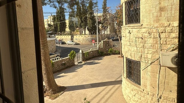 A view through a window with a stone building, a tree, and a clear sky. - Antica Jabalal-lwebdeh 5 (Amman)