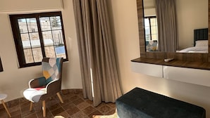 A hotel room with a large window, a chair, a bench, a mirror, and patterned floor tiles.
