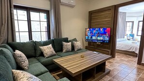 A modern living room with a sectional sofa, a wooden coffee table, a flat-screen TV, and patterned floor tiles.