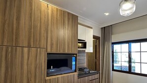 A modern hotel room with a wooden wardrobe, a built-in kitchen area, a bed, and a large window. - 7 Antica Jabalal-lwebdeh (Amman)